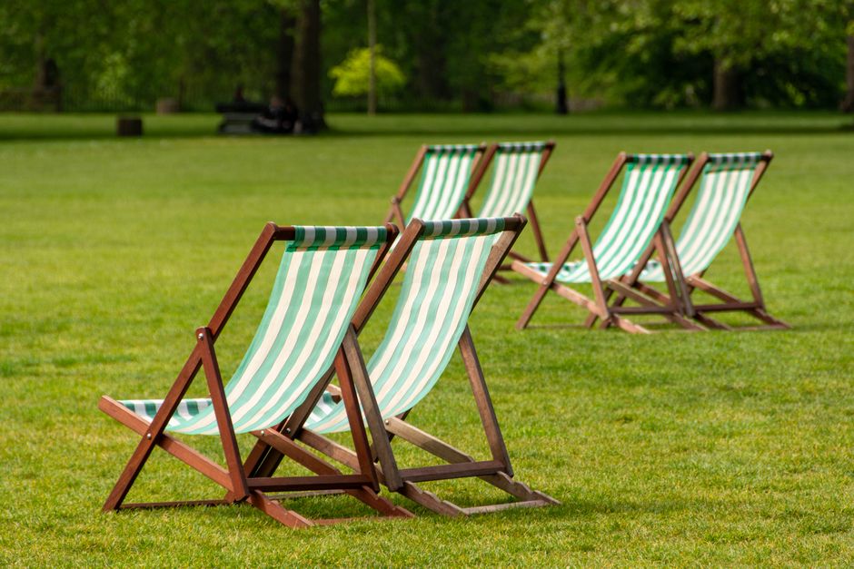 Multiple rows of green upholstered chairs with golden metal frames arranged in an orderly manner in a conference or event room. The chairs are positioned on a carpeted floor, with the lighting appeari